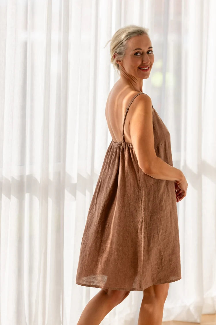 Woman wearing a brown dress standing in front of white curtains