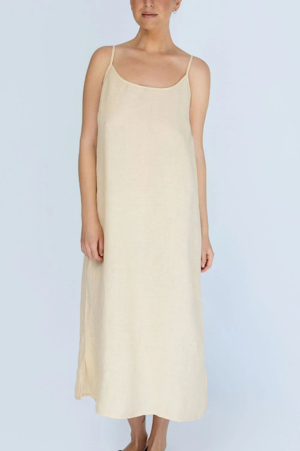 A woman modelling a simple sleeveless midi slip dress in a soft butter yellow colour, set against a solid white background.