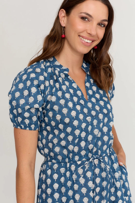 A woman wearing a blue short-sleeve  dress with a white scallop print, featuring puff sleeves and a tie waist, set against a plain light grey background.